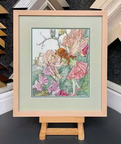 Floral needlework with a peach mount on a display easel framed by Tripps of Keynsham