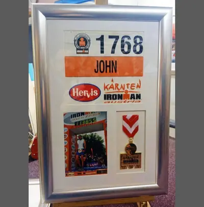 Ironman race number and finisher medal framed together framed by Tripps of Keynsham