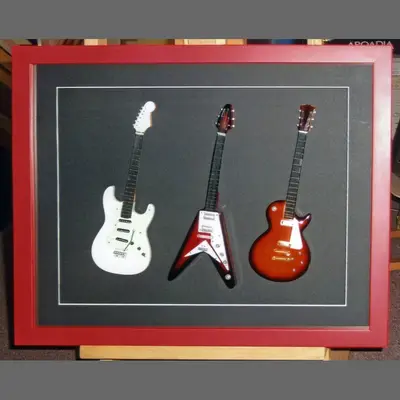 Three miniature guitars in a red box frame framed by Tripps of Keynsham