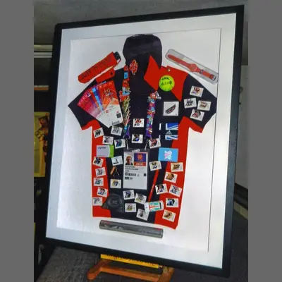 Football shirt covered in pin badges in a white box frame framed by Tripps of Keynsham