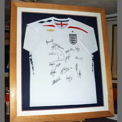 White England football shirt covered in signatures in an oak frame framed by Tripps of Keynsham