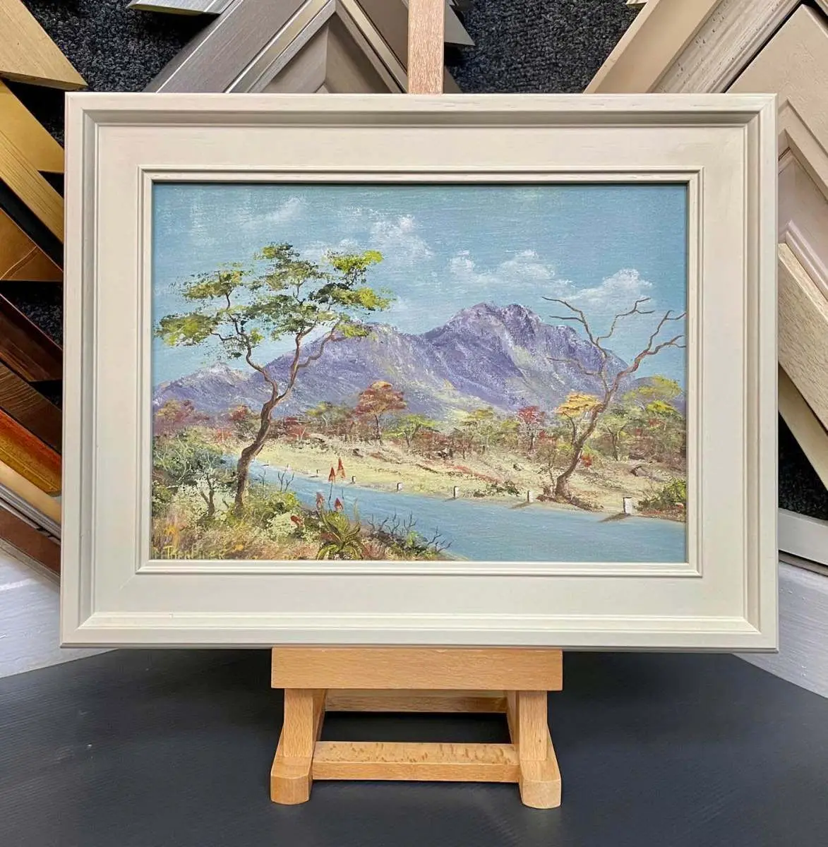 Framed floral oil painting on an easel among frame mouldings at Tripps of Keynsham