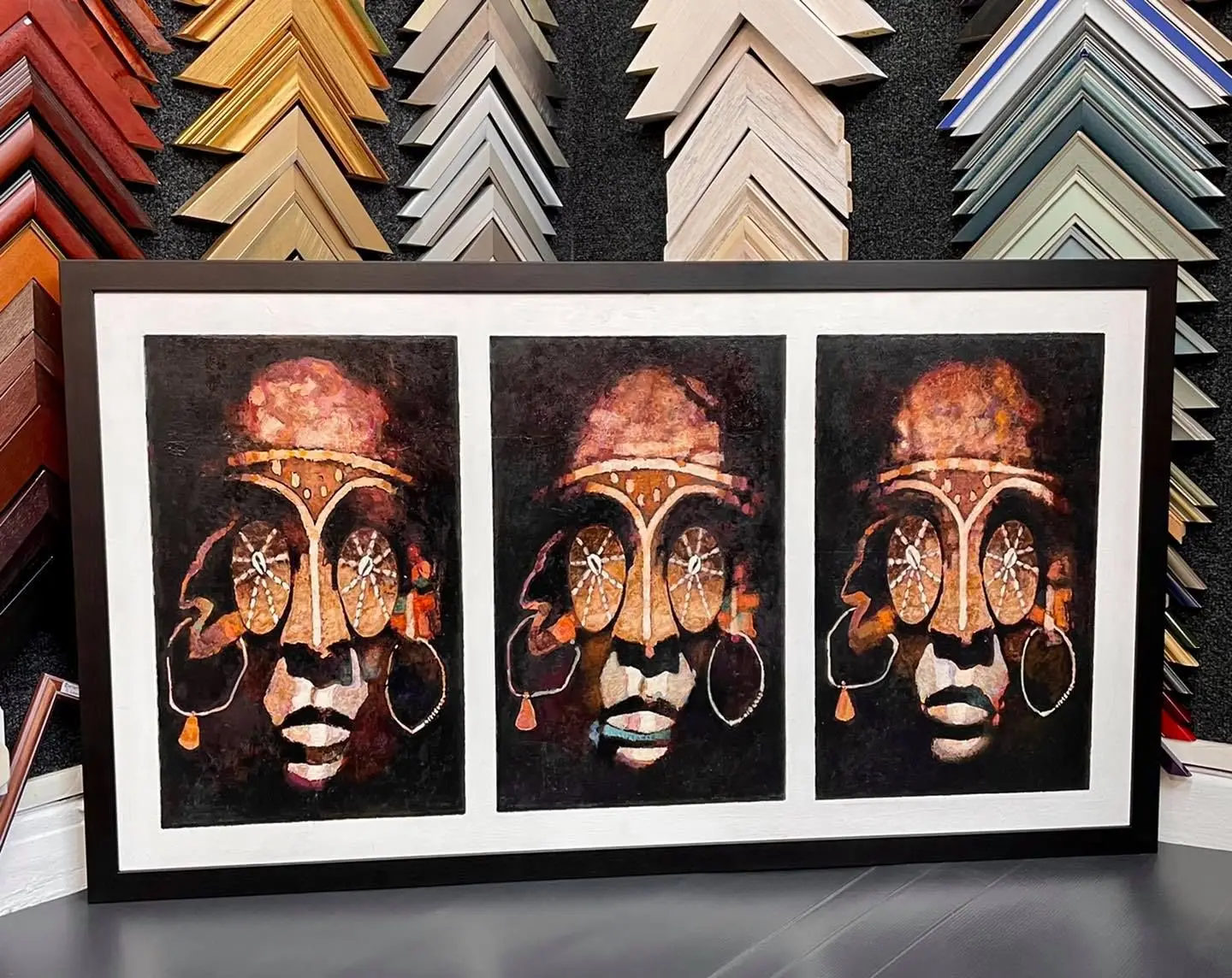 Three framed African mask prints in front of frame moulding samples at Tripps of Keynsham